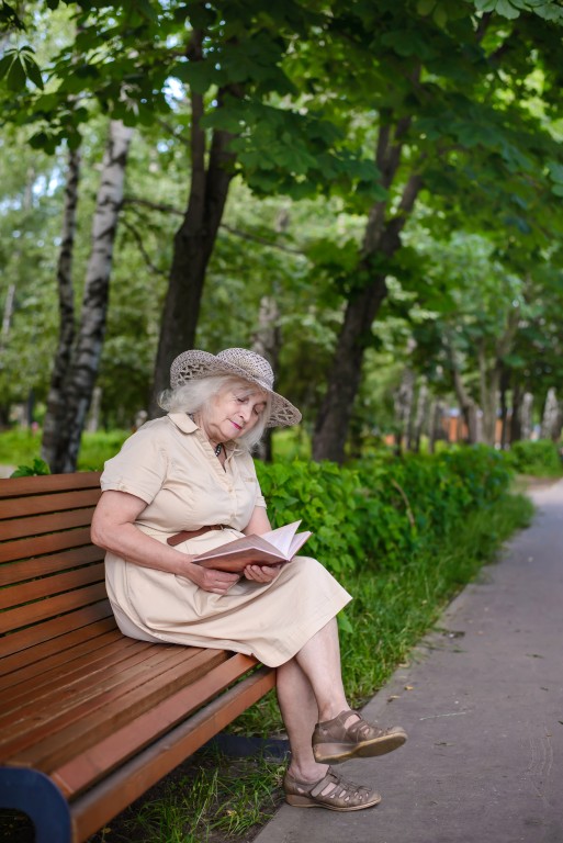 Пожилая женщина читает книгу на лавочке